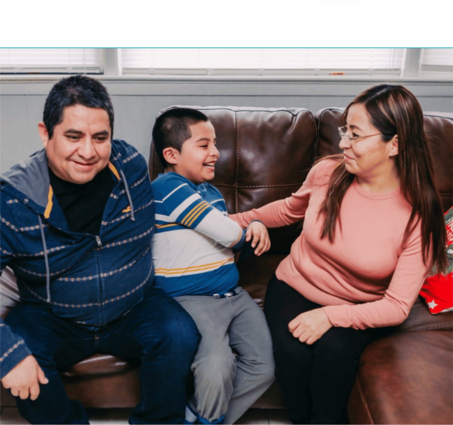 Two adults and two children sitting together on a sofa at home.