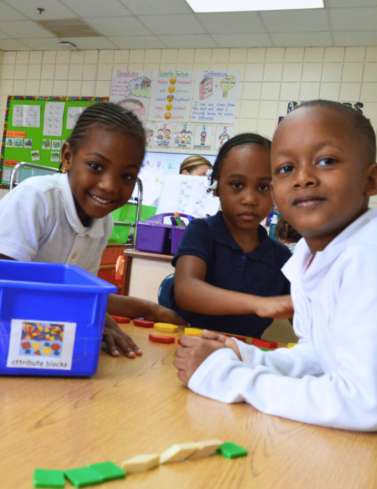 Three young students working with learning materials at a classroom table.