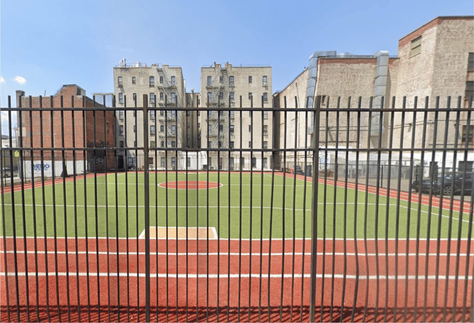 A running track and athletic field enclosed by fencing in front of a large brick building.