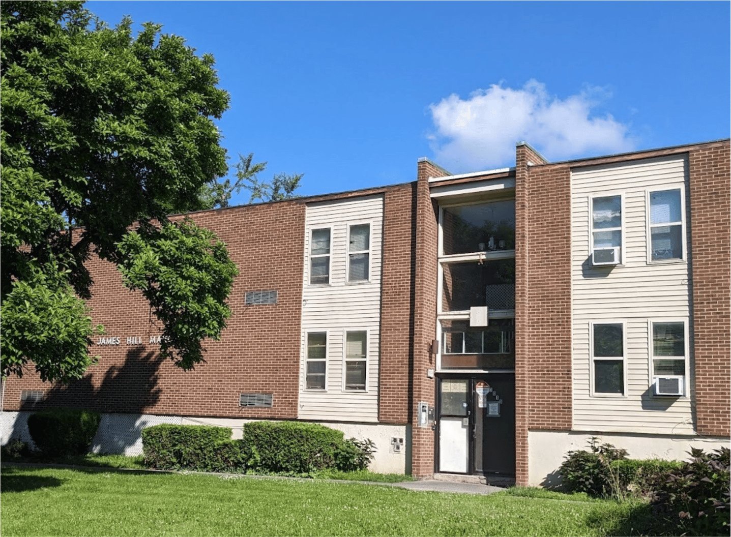 Two multifamily residential buildings with brick and siding facades on a grassy corner lot.