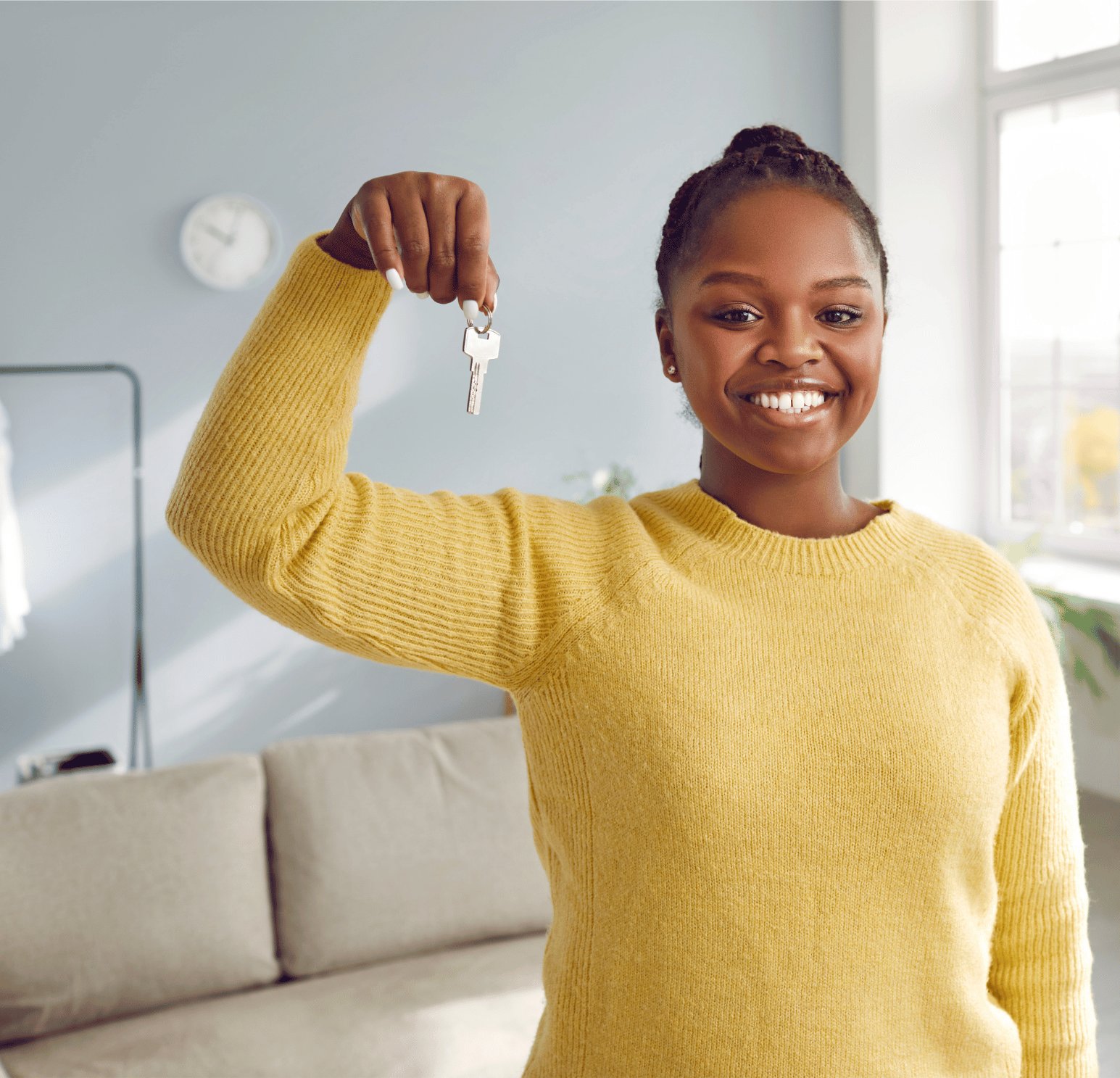 A woman smiling and holding up a set of house keys in a sunlit room.